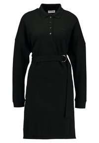 Robe polo noire  à manches longues, avec patte de boutonnage et ceinture à nouer. Fabriquée en tissu doux et texturé avec un petit logo sur la poitrine.