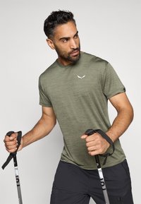 Oliivroheline spordisärk, mis on valmistatud kergest kangast, väike valge logo rinnal ja lühikesed varrukad.