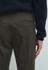 Mørkebrune bukser lavet af glat stof, der har en slim fit, baglommer og en subtil glans, parret med en struktureret marineblå strikket trøje.