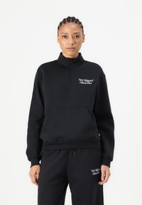 Svart fleece genser med halv glidelås, høy krage, kenguru-lomme, og hvit "New Balance Athlete Club" logo på brystet.