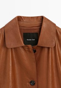 Brun læderjakke med glat tekstur, bred krave og knaplukning. Har et sort indre mærke med "Massimo Dutti" trykt.
