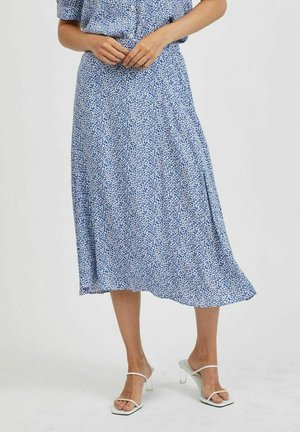 Niebieska spódnica midi w kwiatowy wzór, wykonana z lekkiego materiału, z rozszerzanym dołem i bocznym rozcięciem, zestawiona z białymi sandałami na wysokim obcasie z paskami.