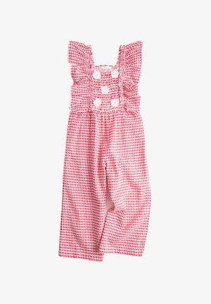 Lächendes Mädchen, das einen rot-weiß karierten Overall mit Rüschen, blumenförmige Sonnenbrillen und beigen Sandalen trägt, steht mit den Händen hinter dem Rücken.