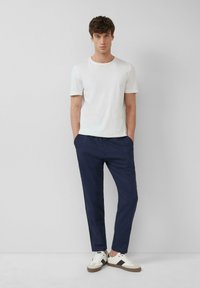 Witte katoenen t-shirt, relaxed fit, gecombineerd met marineblauwe elastische taillebandbroek en witte sneakers met zwarte accenten. Eenvoudig ontwerp.