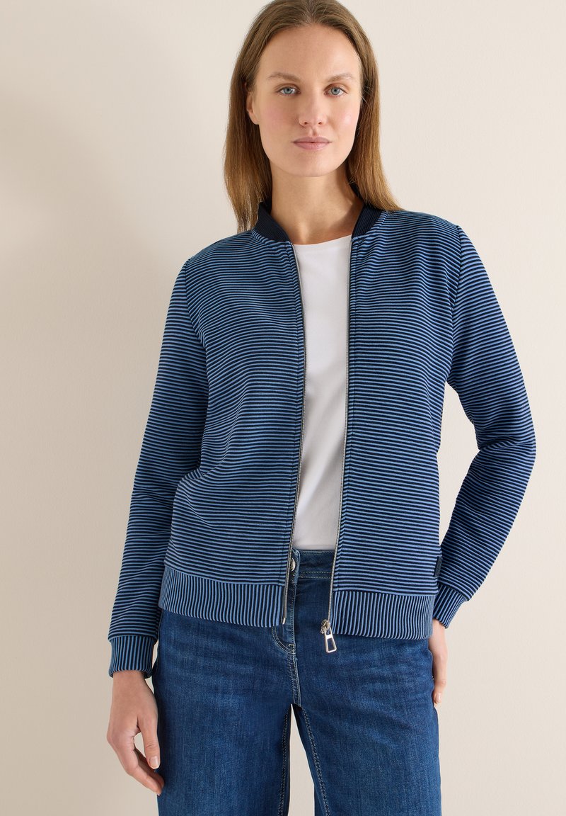 Veste zippée à rayures bleues avec un col et des poignets côtelés, présentant des rayures horizontales contrastantes et une texture lisse.