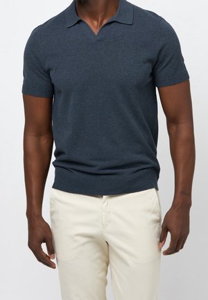 Kortærmet navy polo skjorte lavet af blødt stof, med klassisk krave og tætsiddende kant. Blandet med lyse beige bukser.