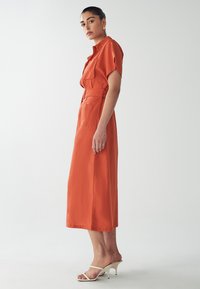 Orange, short-sleeve dress with a belted waist, side pockets, and a flowing maxi length. Smooth texture and modest silhouette.