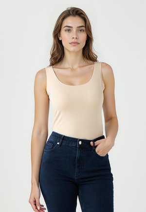 Nude mouwloze bodysuit met een ruime ronde halslijn, gecombineerd met high-waisted donkerdenim jeans met voorkruimels en knoopsluiting.