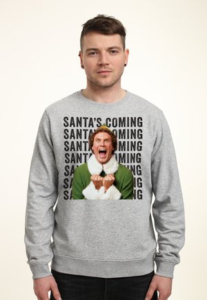Grijze sweatshirt met een centraal grafisch beeld van een personage in een groene outfit met witte accenten. Text leest "SANTA KOMT" in het zwart.