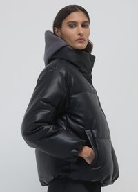 Veste matelassée noire rembourrée en matériau brillant, avec une capuche grise, des boutons-pression et des poches latérales. Texture lisse et design court.