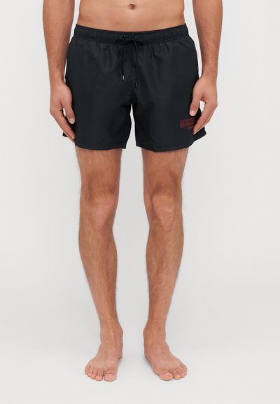 Zwarte zwemshorts van lichtgewicht stof, met een elastische tailleband en trekkoord, en een klein rood logo aan de zijkant.