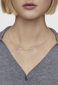 Collana in argento con un design delicato e un piccolo ciondolo, indossata su un maglione grigio, che mette in risalto una superficie liscia e lucente.