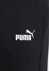 Svarta träningsbyxor i mjukt tyg med en vit Puma-logotyp och silhuett på framsidan, med en slät yta och inga märkbara mönster.