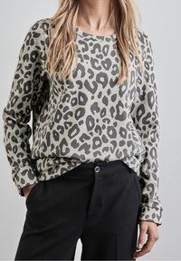 Pull à imprimé léopard en gris et noir, manches longues, col rond, coupe décontractée, fabriqué en tissu doux, associé à un pantalon noir.