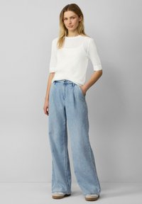 Witte textuur gebreide trui met driekwartmouwen, gecombineerd met hoogtaillight blauwe wijde jeans en beige schoenen.