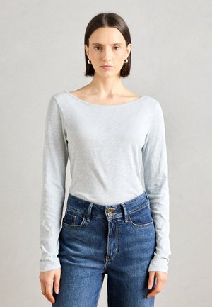 Top gris claro de manga larga hecho de una tela suave, con un escote amplio y mangas ajustadas, combinado con unos vaqueros azul de cintura alta.