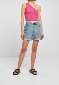 Růžový crop top s jedním ramenním páskem, spárovaný s světle modrými denimovými šortkami s ohrnutými lemy a vysokým pasem. Černé klouzavé sandály.