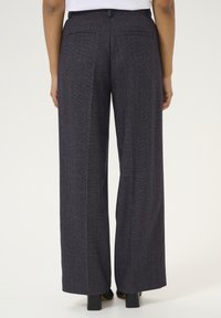 Wide-leg trousers in dark blue fabric with a textured finish. Features two back pockets and a tailored waistband. Black heels worn.
