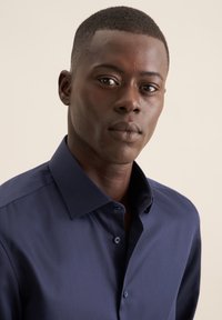 Donker marineblauw overhemd met knopen en een stijve kraag, met een subtiele glans. Het heeft een klassieke pasvorm en blauwe knopen op een lichte achtergrond.