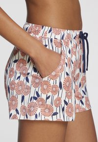 Floral shorts with a drawstring waist, featuring a white background, navy leaves, and peach flowers with circular centers. Visible side pocket.