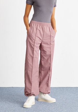Pantalones de pierna ancha, de color rosa claro y fabricados con un tejido texturizado, que cuentan con una cintura elástica y bolsillos en los laterales. Combinados con zapatillas blancas.