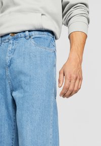 Heledad sinine denim püksid lõdva istuvusega, klassikalise viie taskuga kujundusega ja peene pleekinud tekstuuriga.