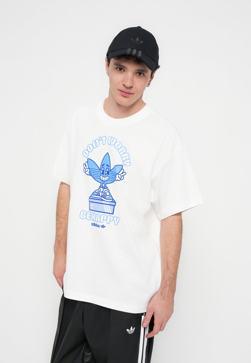 Weißes Baumwoll-T-Shirt mit einer blauen Cartoon-Grafik und dem Text "DON'T WORRY BE HAPPY." Schwarze Kappe mit einem Logo. Schwarze Hose mit weißen Streifen.