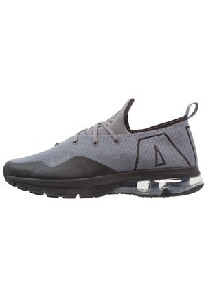 Zapatilla deportiva gris y negra con parte superior de tejido, lengüeta en el talón, cordones y amortiguación visible con aire en la suela.