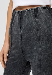 Szare dżinsy z elastycznym paskiem w talii, o miękkiej fakturze i subtelnym, wyblakłym wykończeniu. Gładkie boki bez widocznych detali metalowych.