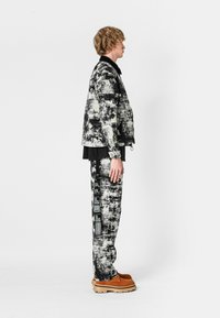 Chaqueta texturizada en blanco y negro y pantalones a juego con detalles gráficos, combinados con calzado de cuero marrón claro. Complementada con una prenda interior negra.