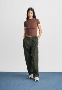 Καφέ εφαρμοστό μπλουζάκι με λευκή επένδυση και λογότυπο Nike, σε συνδυασμό με άνετο πράσινο cargo παντελόνι με πλαϊνές τσέπες και ελαστική μέση.