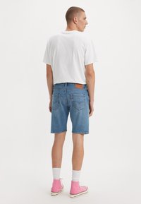 Denim shorts in light blue, featuring five pockets and a leather logo patch. Paired with a white t-shirt and pink high-top sneakers.