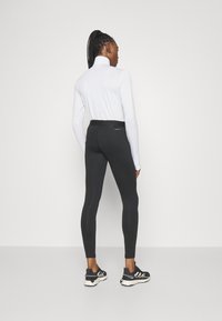 Fekete leggings, szoros fazonnal és elasztikus derékkal, egy hosszú ujjú fehér felsővel párosítva. Simább anyag jellemzi, és nincsenek látható minták.