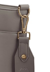 Detail šedé kožené tašky, který ukazuje zlatý kovový zámek, prošitou stuhu a kulatou logo knoflík. Hladká textura s pevným tvarem.