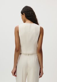 Haut sans manches de couleur crème avec des rayures verticales, un décolleté droit au dos et une silhouette ajustée, associé à un pantalon fuselé.