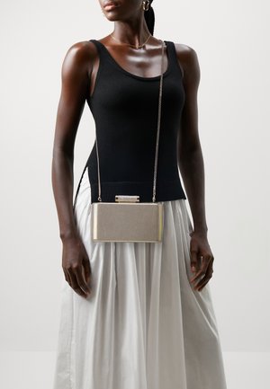Metallic gold clutch with a textured finish and clasp. Worn on a chain strap; paired with a black tank top and white skirt.