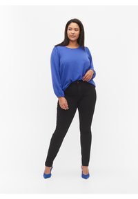 Top azul de manga larga con tejido texturizado, combinado con jeans skinny negros y tacones azules, presentando un diseño ajustado y detalles sutiles.
