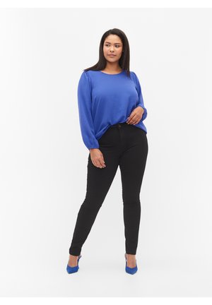Blaue Langarmbluse aus strukturiertem Stoff, kombiniert mit schwarzen Skinny-Jeans und blauen High Heels, mit taillierter Passform und subtilen Details.