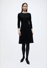 Μαύρο φόρεμα με μανίκια τριών τετάρτων, εφαρμοστή γραμμή, στρογγυλή λαιμόκοψη και φουσκωτή φούστα. Συνδυασμένο με μαύρο καλσόν και ψηλοτάκουνα με μυτερή μυτούλα.