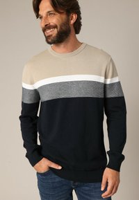 Pull en tricot avec des blocs de couleur horizontaux en beige, blanc, gris et bleu marine. Col rond, manches longues et poignets et ourlet côtelés.
