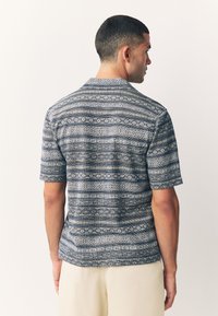 Kurzärmeliges Hemd aus dunkelblauem Stoff mit komplexen weißen und hellblauen geometrischen Mustern und einem entspannten Kragen-Design.