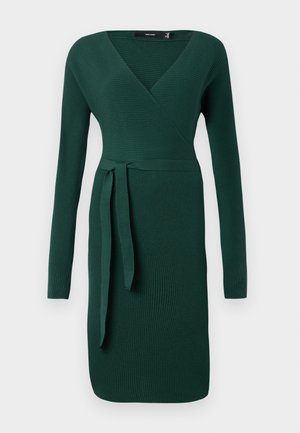 Mørkegrønn, ribbet langermet kjole med v-hals og et belteaksent ved midjen. Figursydd design med knelengde.