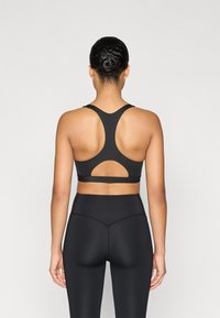 Sujetador deportivo negro con diseño de espalda racer y detalle de recorte, combinado con leggings negros de cintura alta con un sutil patrón texturizado.
