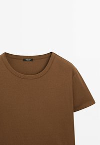 T-shirt marron à manches courtes et col rond sur fond blanc, montrant la partie supérieure avant et la zone de l'épaule.