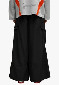 Pantaloni cargo neri a gamba larga con tasche laterali e finitura testurizzata, abbinati a una maglia grigia a maniche lunghe con dettagli e grafiche arancioni.