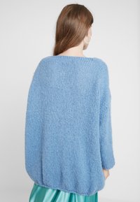 Ljusblå, oversized stickad tröja med lös passform, vida ärmar och texturerat tyg. Fållen är något kortare nedtill.