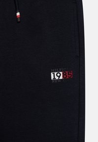 Námořnické tepláky vyrobené z měkké tkaniny, s vyšitým logem "HILFIGER 1985 NEW YORK" v bílé, červené a černé barvě. Pas na šňůrku.