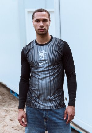 Ilgų rankovių sportinis marškinėlis su juodai pilku dryžuotu dizainu, Nike logotipu ir liūto emblema ant krūtinės, pagamintas iš sklandžios, lengvos medžiagos.