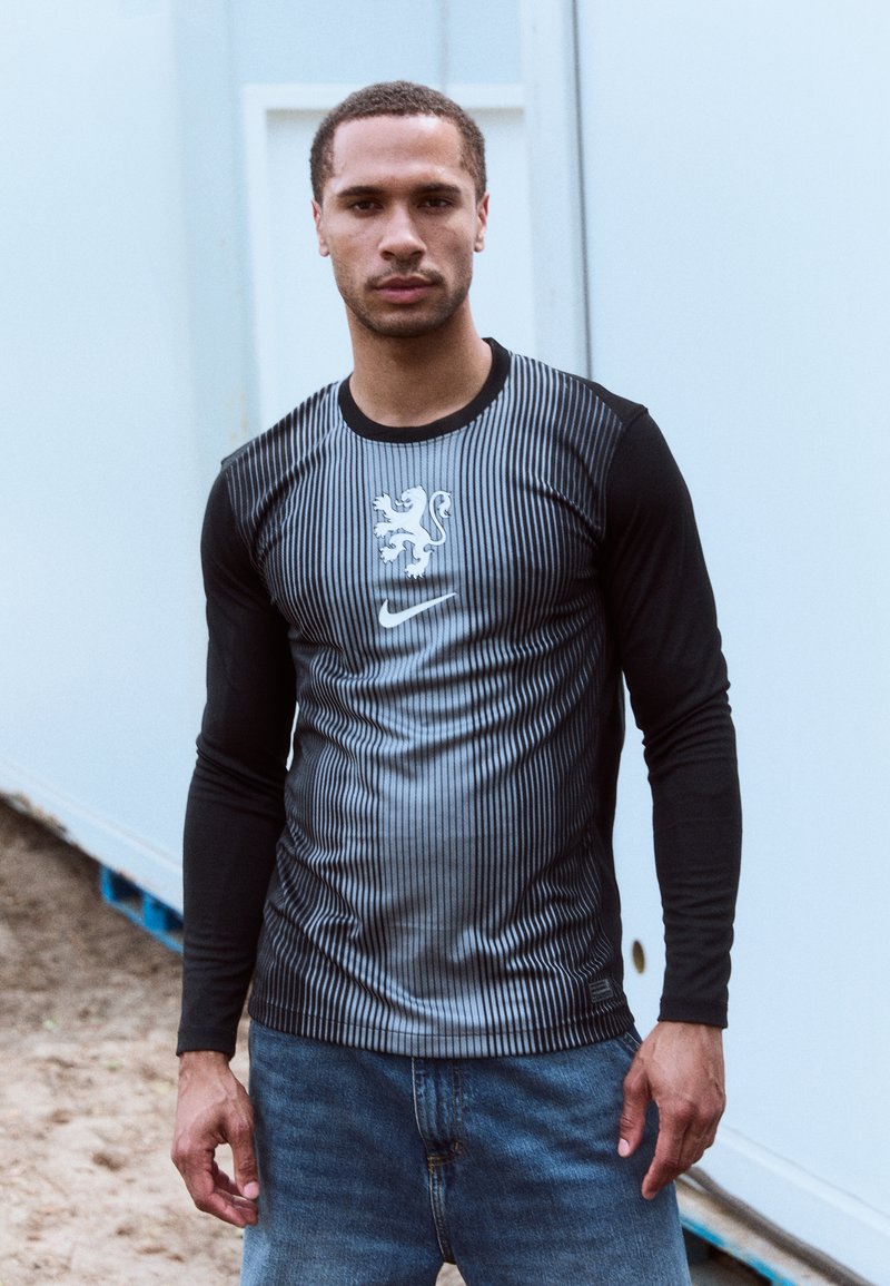 Langsleeve sportshirt met een zwart en grijs gestreept ontwerp, Nike-logo en leeuwembleem op de borst, gemaakt van dun, lichtgewicht materiaal.