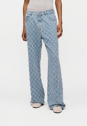 Lyseblå denimjeans med et diamantmønster af perle-lignende perler, båret med lys beige sko og en hvid top.